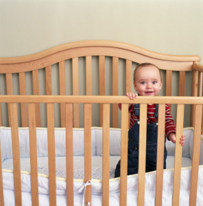 Baby boy (9-12 months) standing in crib, smiling, portrait